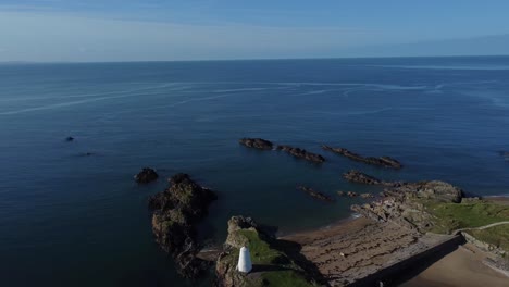 Establishing-aerial-view-Ynys-Llanddwyn-island-lighthouse-and-beacon-on-calm-Irish-sea-at-sunrise