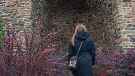 Girl-with-long-hair-walks-between-red-bushes-to-a-stone-wall-in-slow-motion