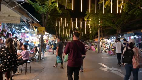 A-car-coming-down-and-shoppers-walk-around-the-sidewalks-to-look-for-what-they-want-to-buy-and-eat-at-the-famous-Chatuchak-Weekend-Market-in-Bnagkok,-Thailand