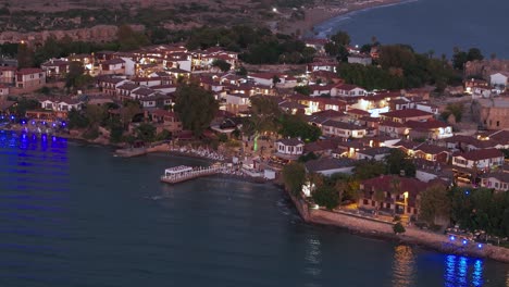 Aerial-view-flying-across-Side-old-town,-Turkey-illuminated-waterfront-neighbourhood-homes-and-marine-coastline