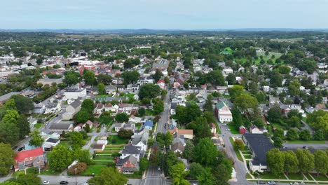 Aerial-view-of-picturesque-suburban-town-with-a-patchwork-of-residential-houses,-tree-lined-streets,-set-against-a-backdrop-of-green-fields-and-distant-hills
