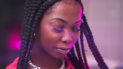 cinematic-close-up-of-black-African-model-wearing-silver-braids-jewellery-covered-with-purple-light-film-like-blurred-background-inside-a-bathroom-checking-herself-in-mirror-touching-hair-looking-nice