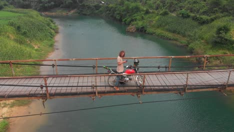 Man-is-standing-with-motorbike-on-old-suspension-bridge-at-Vietnam,-aerial