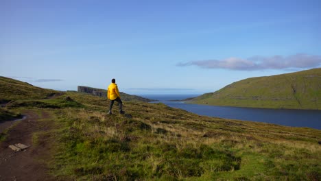 Man-in-yellow-raincoat-admiring-the-green-and-volcanic-Faroese-landscape-in-Leitisvatn