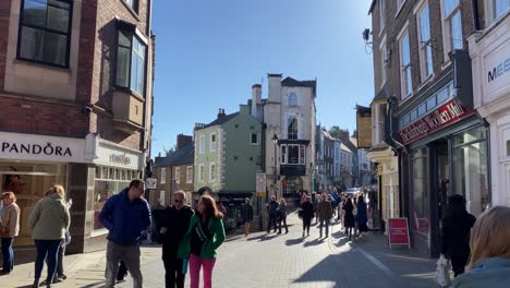 A-POV-shot-of-Saddler-Street-in-Durham-City,-full-of-people-on-a-bright-sunny-day-with-clear-blue-skies