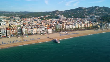 Air-of-the-main-beach-of-Lloret-De-Mar-recorded-with-Drone-passenger-boat,-people-boarding-on-the-beach