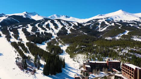 Snow-Covered-Ski-Slope-Trails-at-Giant-Winter-Resort-with-People-Skiing-and-Riding-Chairlifts-Down-Mountain-through-a-Pine-Tree-Forest-and-Snow,-Aerial-Drone-View