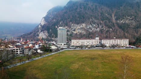 Drone-rises-above-leafless-trees-to-reveal-hotel-and-homes-of-Interlaken-Switzerland-on-cloudy-day