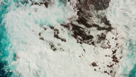 Top-down-aerial-drone-shot-of-waves-splashing-against-the-rocks-at-the-shore