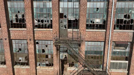 Close-up-view-of-old-brick-industrial-building-facade-with-shattered-windows-and-a-rustic-metal-fire-escape,-conveying-urban-decay-and-historical-architecture
