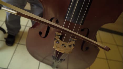 close-up-of-a-contrabass-cello-bass-and-a-man-wearing-black-sandals-holding-a-stick-to-make-the-sound-baroque-era-classical-royal-sounds-played-inside-kingdom-palace-for-important-people-man-standing