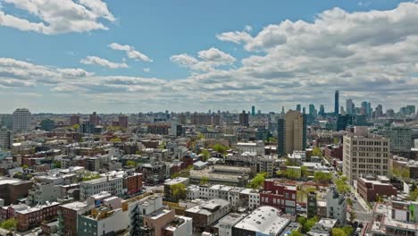 Drone-flyover-american-neighborhood-in-Brooklyn-and-skyscraper-in-background-during-sunny-day---NYC,-America