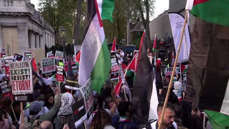 Cientos-De-Personas-Se-Reúnen-En-La-Calle-Frente-A-La-Embajada-De-Israel-En-Londres-Sosteniendo-Banderas-Palestinas-Y-Pancartas-De-Protesta-Mientras-El-Rapero-Low-Key-Dirige-Cánticos-Políticos-En-Un-Escenario.