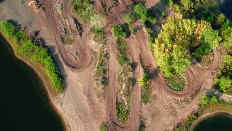 Aerial-drone-top-down-view-of-a-motocross-track-nestled-within-a-scenic-lake