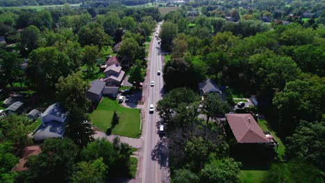 Aerial-drone-shot-follows-a-straight-road-surrounded-by-American-houses-adorned-with-lush-green-gardens-in-an-American-neighborhood