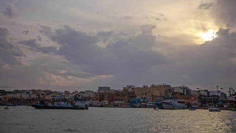 Zeitraffer-Vor-Der-Küste-Des-Romantischen-Fischerdorfes-Marsaxlokk-Auf-Der-Urlaubsinsel-Malta-Mit-Blick-Auf-Die-Schwimmenden-Frachtschiffe-Und-Fischerboote-Sowie-Die-Historischen-Gebäude