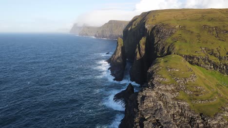 Distant-drone-footage-of-steep-cliffs-with-a-rising-sun-near-the-Leitisvatn-Lake,-aka-the-Floating-Lake,-on-the-Vagar-island-in-the-Faroe-Islands
