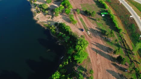 A-top-down-aerial-drone-shot-follows-two-motocross-bikes-as-they-speed-around-a-motocross-circuit-next-to-a-picturesque-lake-in-the-United-States,-USA