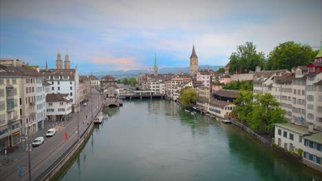 Zurich-Switzerland-Aerial-Pull-Back-Up-Establishing-Shot-Church-Europe-Water-River-Stream-Statue-Bridge-Europe-Steeple-Walkway-People-Urban-Architecture-4K-60-Fps-Tourist-Destination-View-Swiss-Town