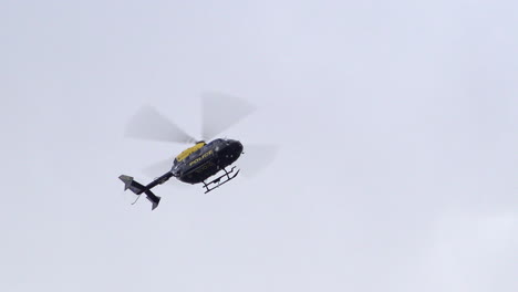 As-a-police-helicopter-moves-back-and-forth-while-hovering-in-a-cloudy-sky-the-crew-can-been-seen-looking-out-the-windows