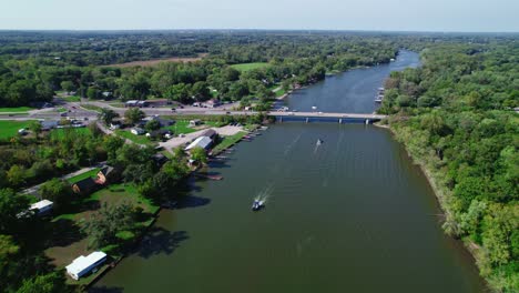 Aerial-View-Landscape-over-the-Fox-River-with-Boats-Passing-by-and-Bridge-with-some-Traffic,-Crystal-Lake,-Illinois