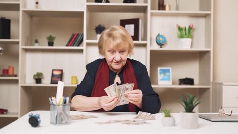 elderly-woman-happily-counts-dollar-bills,-arranging-them-on-the-table