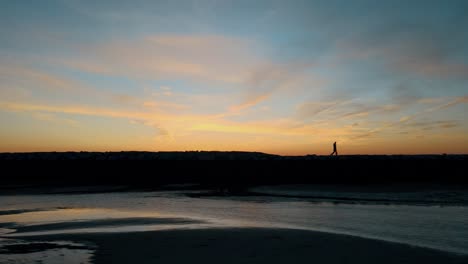 Aerial-view-showing-Silhouette-of-couple-Walking-on-dam-in-Provincetown-during-golden-sunset---Breakwater-of-Atlantic-Ocean-in-America---lateral-flight