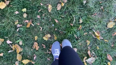 Woman-in-black-leggings-with-bright-sport-shoes-walks-along-grassy-with-fallen-leaves