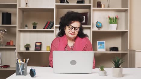 old-woman,-with-a-sad-expression,-finishes-her-work-on-the-laptop-and,-taking-off-her-glasses,-massages-her-neck