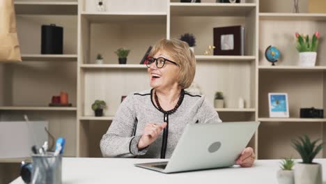 older-woman-in-glasses-orders-food-delivery-online-while-sitting-behind-her-laptop,-and-the-courier-swiftly-delivers-it,-leaving-the-woman-impressed-and-smiling