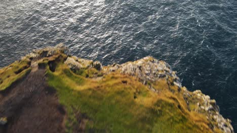 Drone-footage-passing-by-grass-with-a-ruin-and-text-written-with-rock-and-a-very-steep-cliff-on-the-Vagar-island-in-the-Faroe-Islands