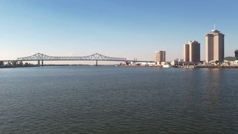 Eine-Luftdrohne-Fliegt-über-New-Orleans-In-Richtung-Der-Crescent-City-Connection-Bridge-Entlang-Des-Mississippi-River-Und-Passiert-Dabei-Gebäude-Auf-Der-Rechten-Seite