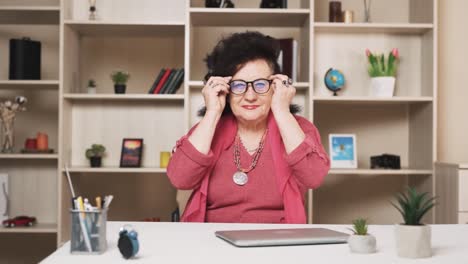 old-woman-puts-on-glasses-and,-opening-a-laptop,-starts-working-and-smiling-at-the-camera