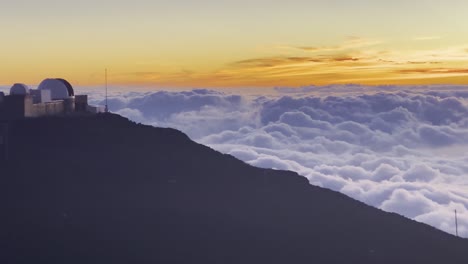Cinematic-panning-shot-from-the-Haleakala-Observatory-to-the-rolling-clouds-below-the-summit-of-Haleakala-at-sunset-in-Maui,-Hawai'i