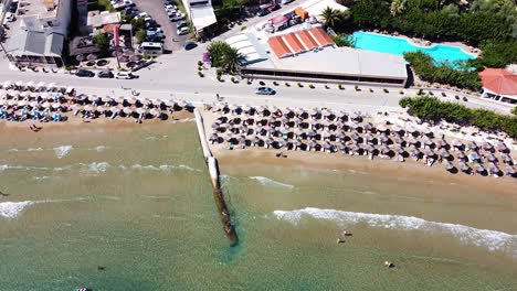Breakwater-and-umbrellas-on-sandy-beach-on-Crete-coast,-aerial-view