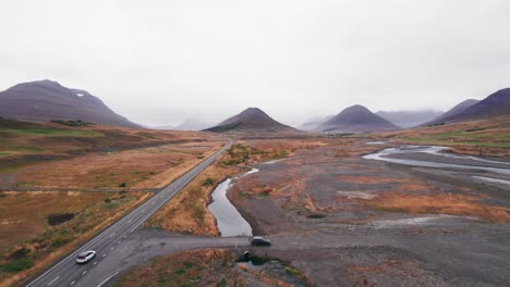 Aerial:-Reveal-and-following-white-SUV-traveling-along-the-Iceland-Ring-Road-which-is-a-scenic-highway-through-a-picturesque-remote-fjord-area-leading-to-twin-peaks-with-fog-and-haze-in-the-distance