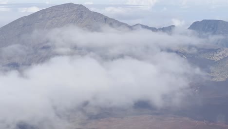 Cinematic-close-up-panning-shot-of-thick-clouds-blanketing-the-volcanic-crater-at-the-summit-of-Haleakala-in-Maui,-Hawai'i