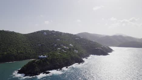 Captivating-aerial-view-circling-virgin-island-usvi-white-sand-beach-blue-water-sky-white-clouds-turquoise-water-with-homes-on-the-mountain-cliff