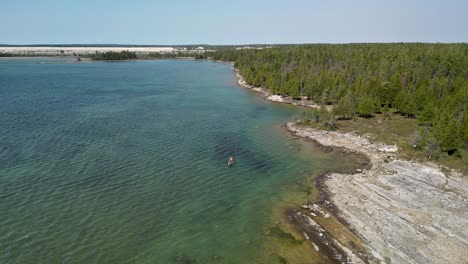 Aerial-view-of-family-canoeing-along-glacier-groove-coastline,-Bush-Bay-Wilderness,-Les-Cheneaux-Islands,-Michigan