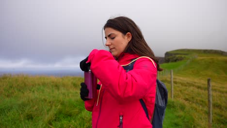 Close-up-of-young-woman-on-a-hike-drinks-hot-beverage-in-Faroe-Islands-landscape