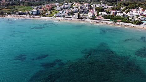 Crystal-clear-sea-water-and-small-cozy-township,-aerial-view