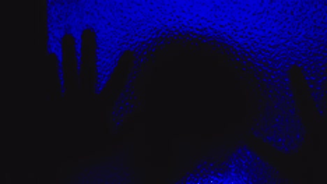 Die-Gruselige-Silhouette-Eines-Besessenen-Mannes-Kriecht-Im-Dunkeln-Unter-Dem-Eindringlichen-Blauen-Licht-Auf-Glas
