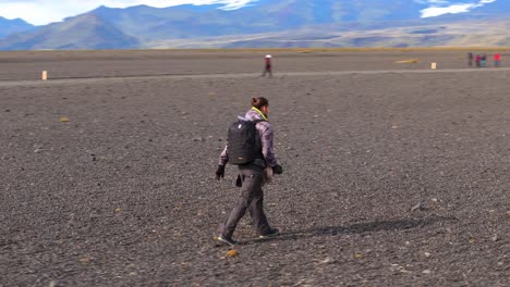 Drone-rotation-around-a-tourist-traveler-walking-in-the-desert-landscape-of-Iceland,-he-is-equipped-with-a-camera-bag