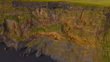 Eine-Neigbare-Luftaufnahme-Zeigt-Einen-Schwarzen-Vulkansandstrand-Unterhalb-Der-Klippe-In-Island