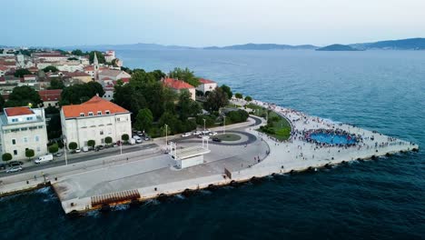 Aéreo-Sobre-La-Costa-Del-Mar-Del-Monumento-Al-Atardecer-De-Zadar,-También-Conocido-Como-El-Monumento-Al-Sol,-Una-Instalación-De-Arte-Cautivadora-E-Innovadora-Ubicada-En-La-Hermosa-Ciudad-Croata-De-Zadar