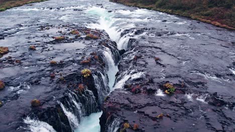 Luftaufnahme:-Nahaufnahme-Des-Bruarfoss-Wasserfalls-Im-Süden-Islands,-Der-Mit-Der-Wunderschönen-Blauen-Kaskade-Von-Wasserfällen,-Die-In-Das-Darunter-Liegende-Tauchbecken-Münden,-Sehr-Malerisch-Ist