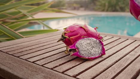 Man-takes-a-piece-of-dragon-fruit-with-a-swimming-pool-in-the-background