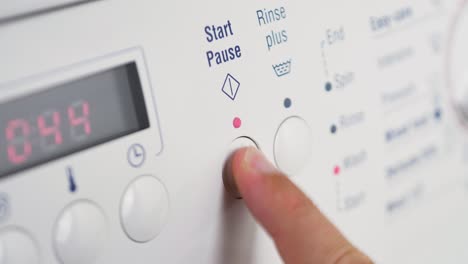 Close-up-shot-of-slow-motion-finger-pressing-start-pause-button-on-washing-machine-dial-rinse-clothing-cleaning-laundry-detergent-household-4K