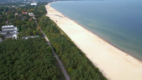 A-stunning-aerial-view-of-Jetikowo-Beach-in-Gdansk,-with-lush-greenery,-a-long-white-sandy-beach,-and-crystal-clear-blue-waters-on-a-sunny-day