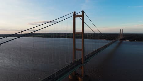 Serenity-meets-motion:-Humber-Bridge-basks-in-sunset's-glow,-with-an-aerial-drone-capturing-cars-in-harmonious-transit